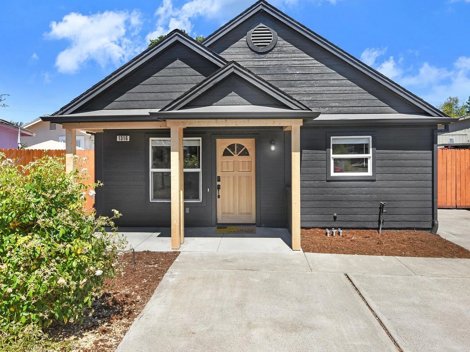 Front view of a dark gray house with a beige door, small porch, and concrete driveway under a blue sky