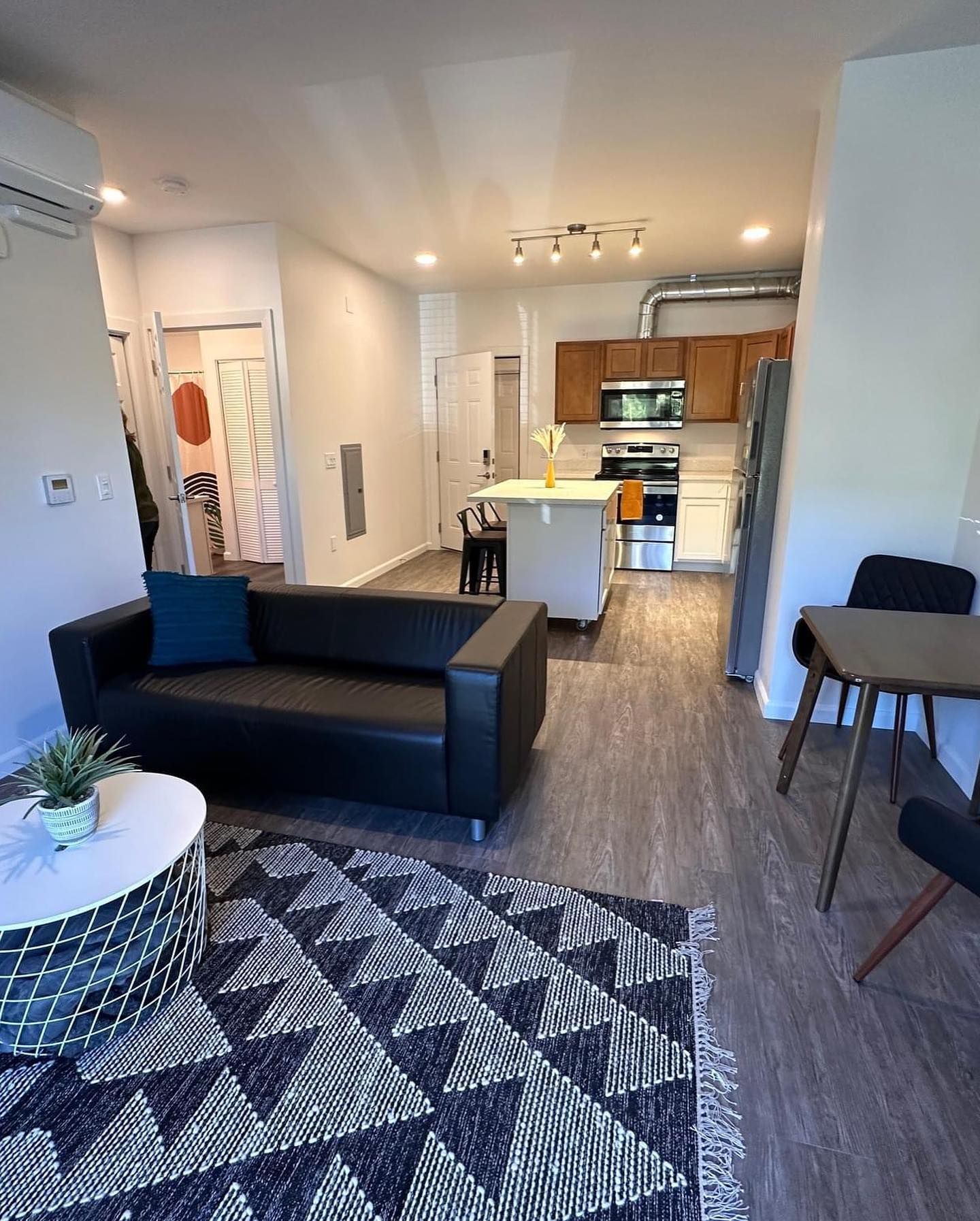 Modern open-plan living room and kitchen with black sofa, patterned rug, and dining table