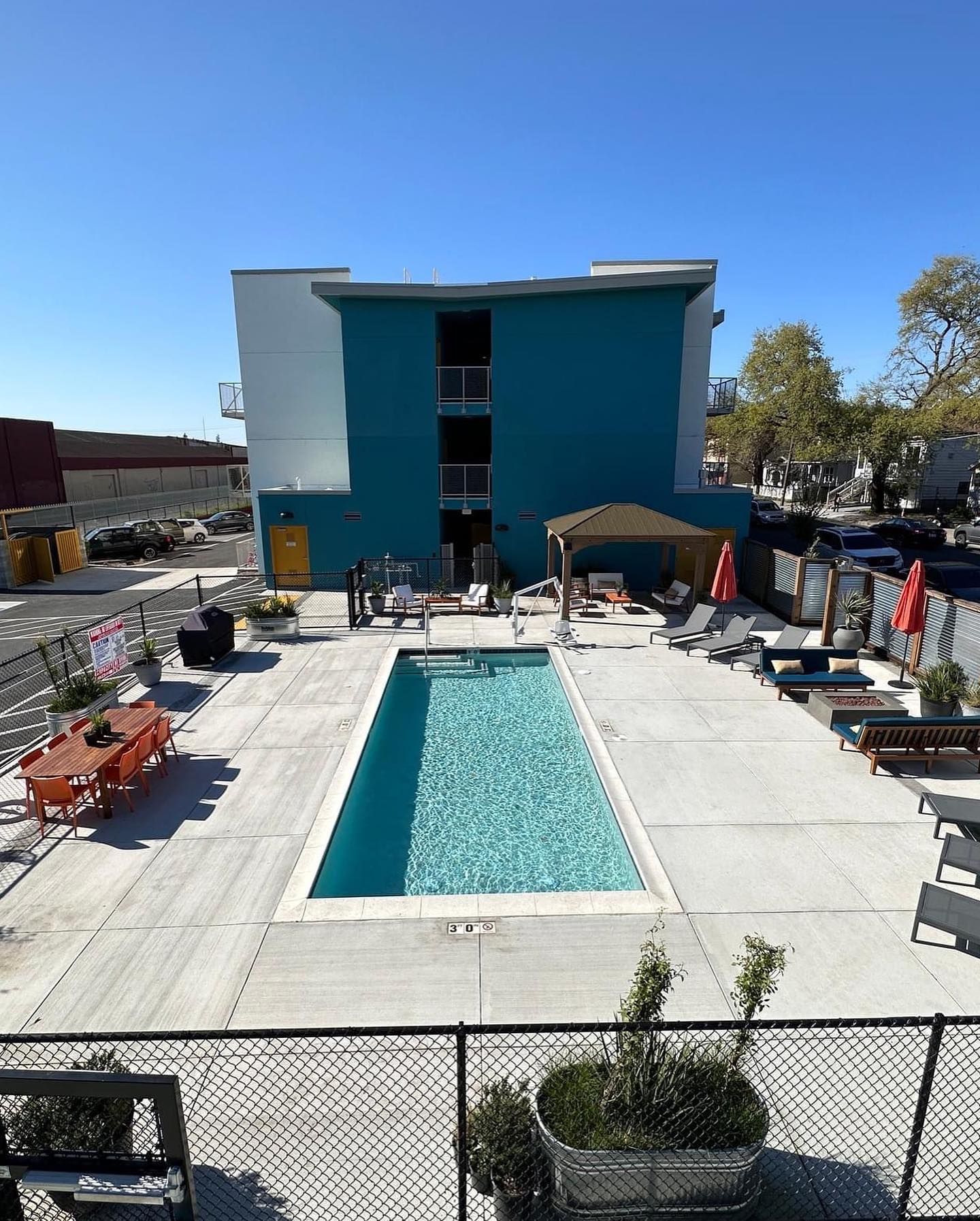 Outdoor pool courtyard with lounge chairs beside a blue-and-white building under a clear sky
