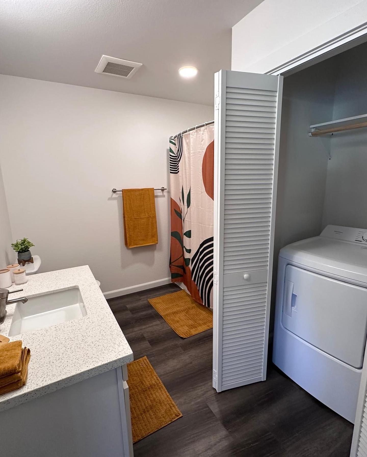 Bathroom with vanity, towel rack, shower curtain, and open laundry closet with washer and dryer.