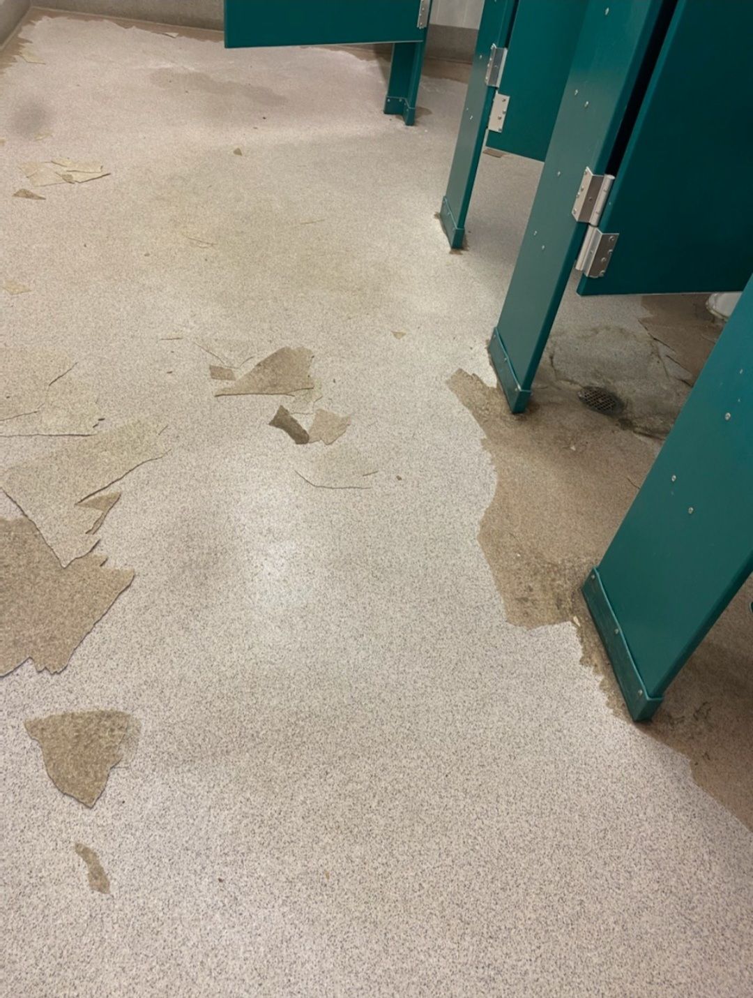 Wet beige floor with puddles beside teal restroom stalls