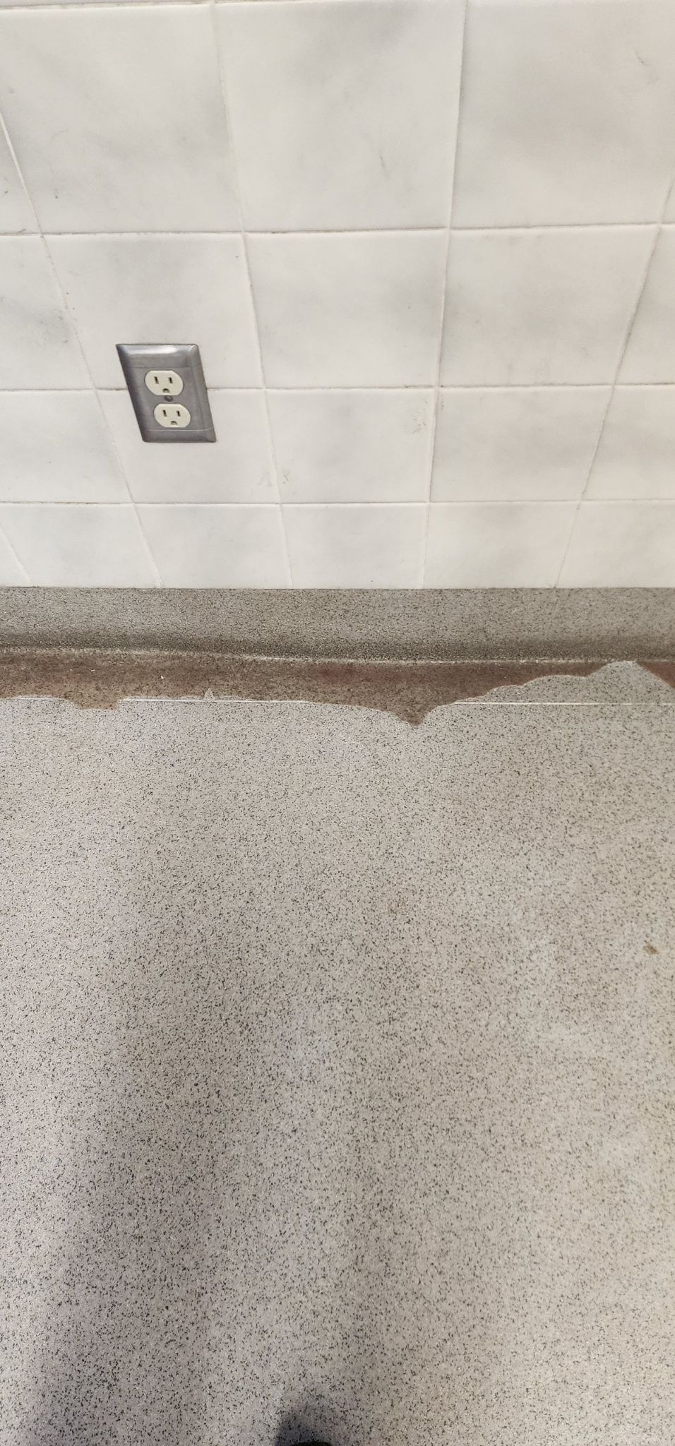 Wall with an electrical outlet above a speckled countertop edge