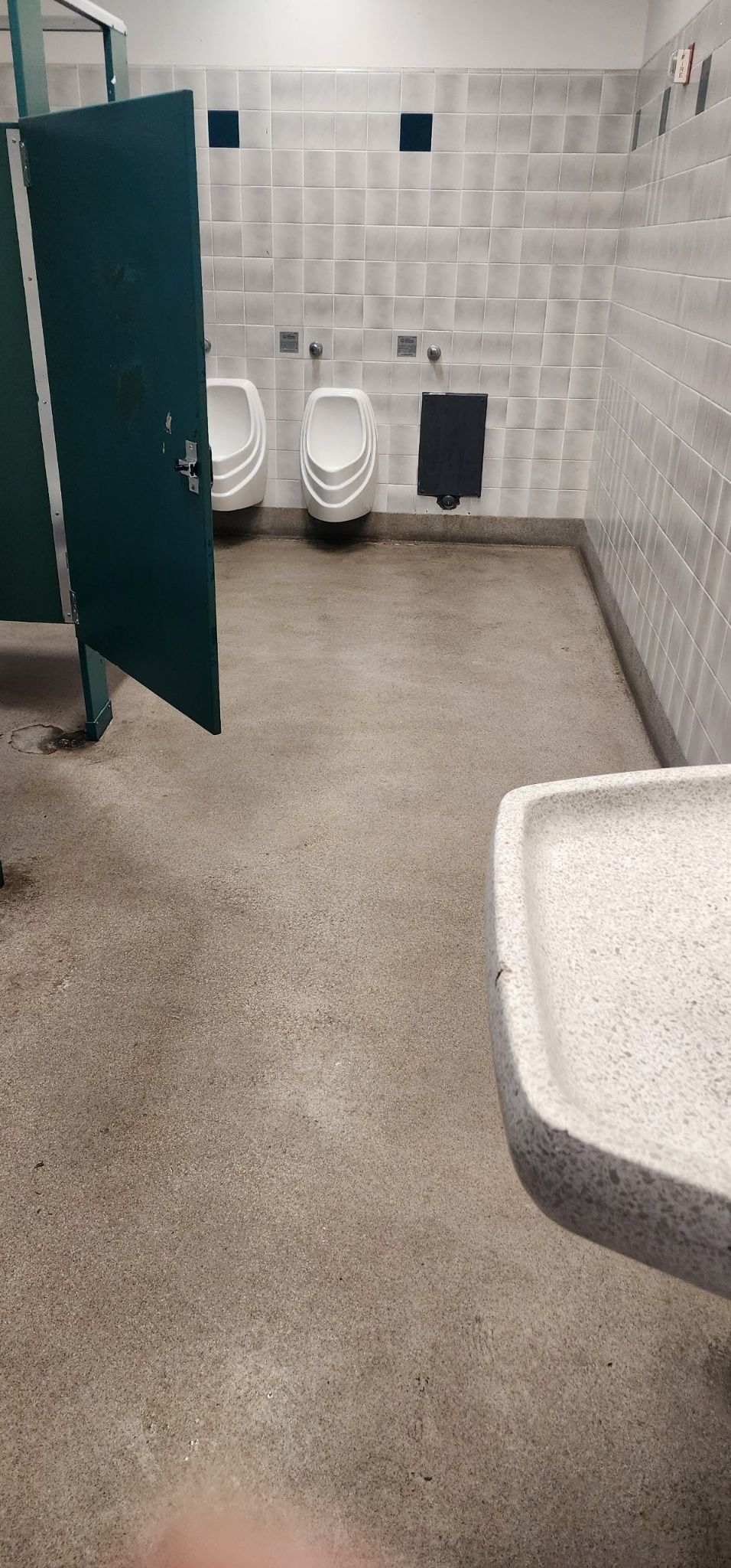 Public restroom with open stall door, urinals, tiled walls, and a sink in the foreground