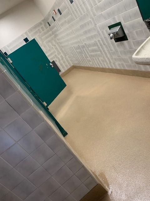 Public restroom stall with teal door, beige floor, and white tiled walls.