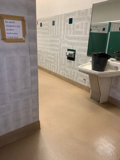 Public restroom with tiled walls, green stall doors, a sink, and a black bucket on the counter