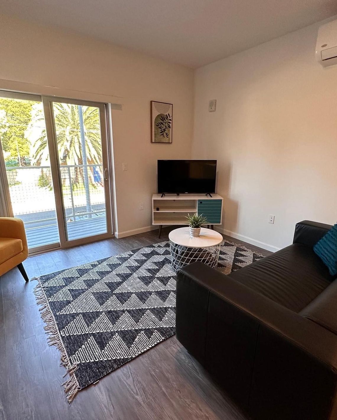 Modern living room with dark sofa, patterned rug, TV, coffee table, and sliding glass door to patio.
