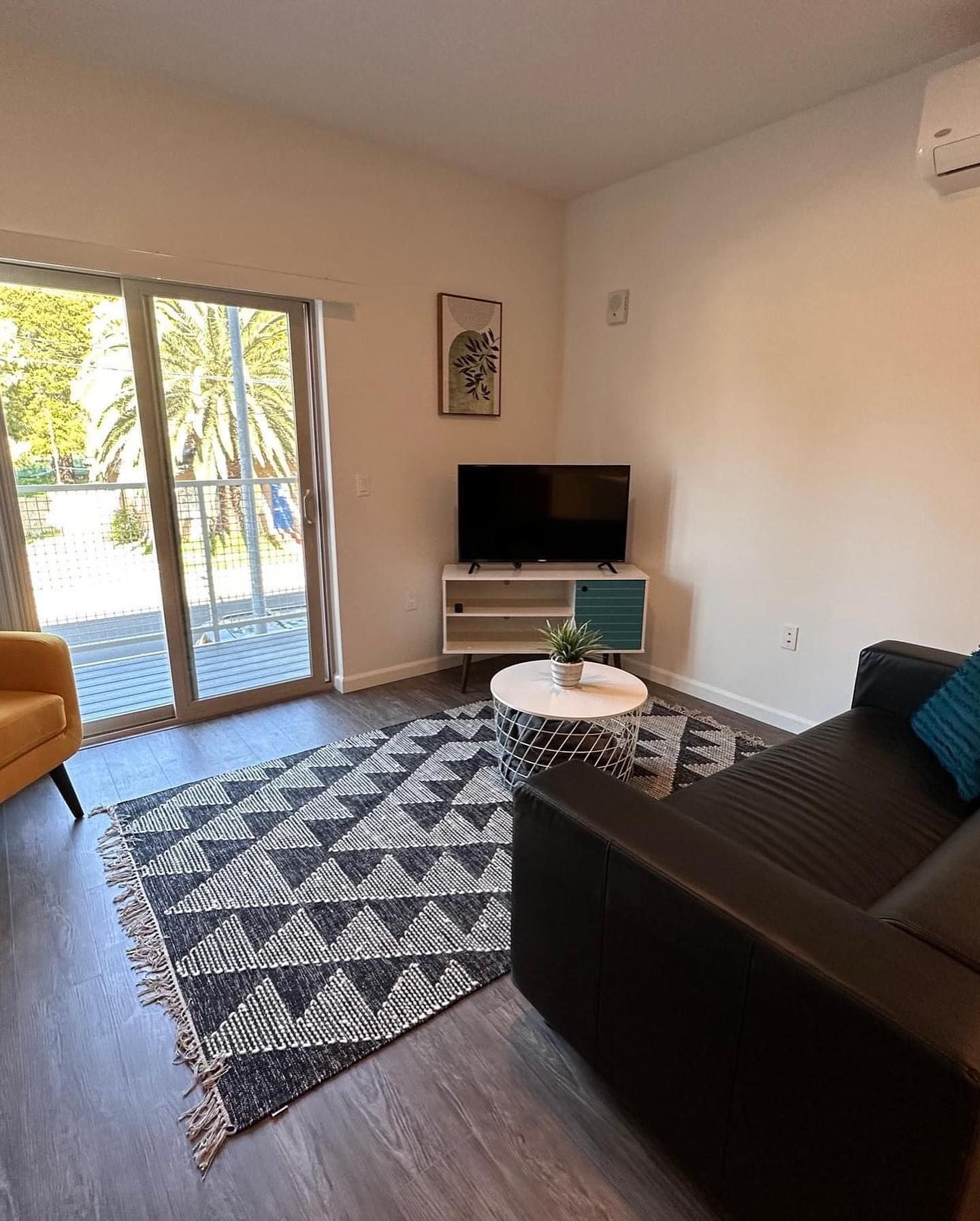 Modern living room with dark sofa, patterned rug, TV, coffee table, and sliding glass door to patio.