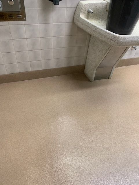Public restroom floor with a wall-mounted sink and beige tile walls.