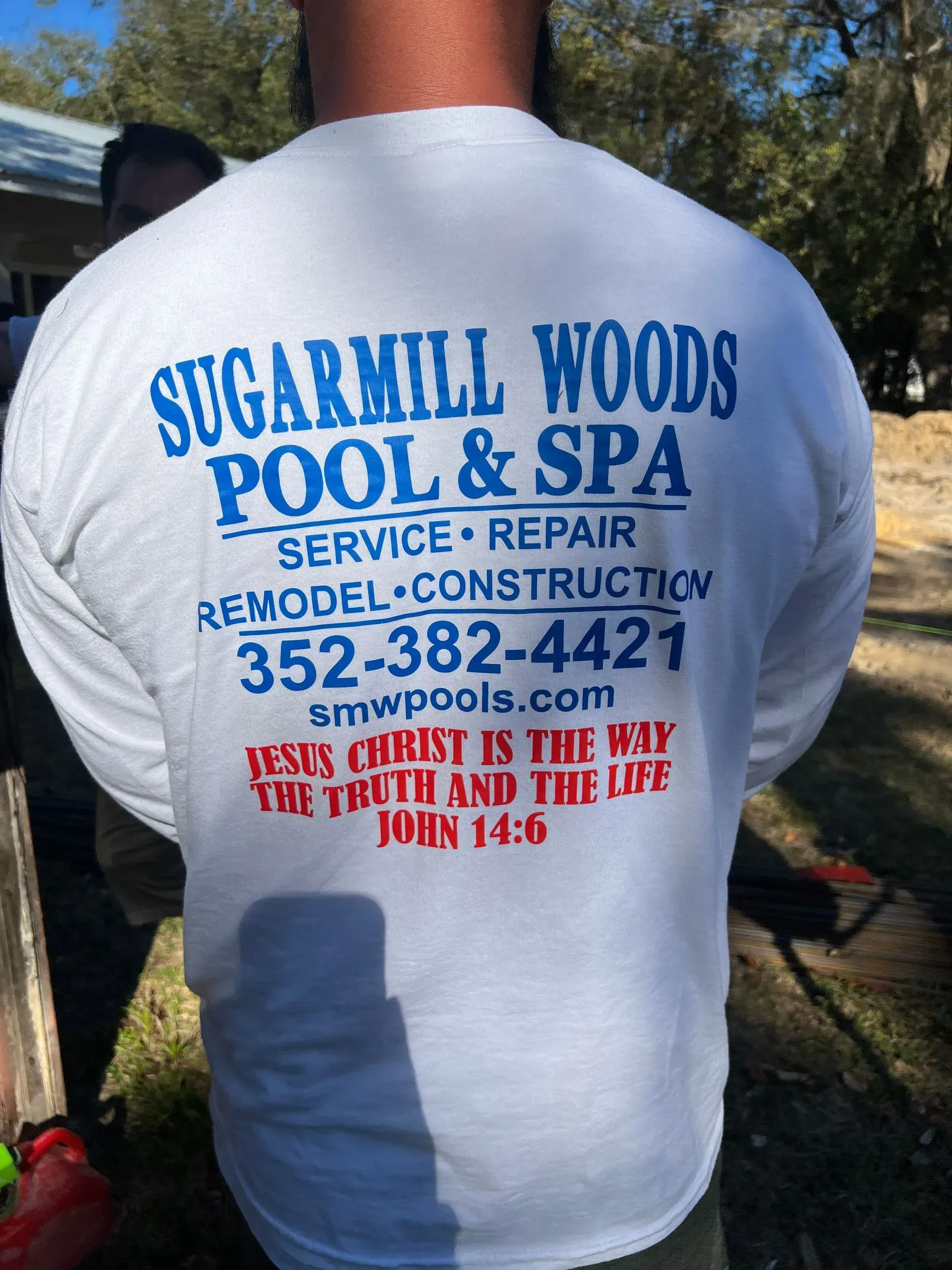Man's back wearing a white shirt advertising Sugarmill Woods Pool & Spa, phone number, and bible verse.