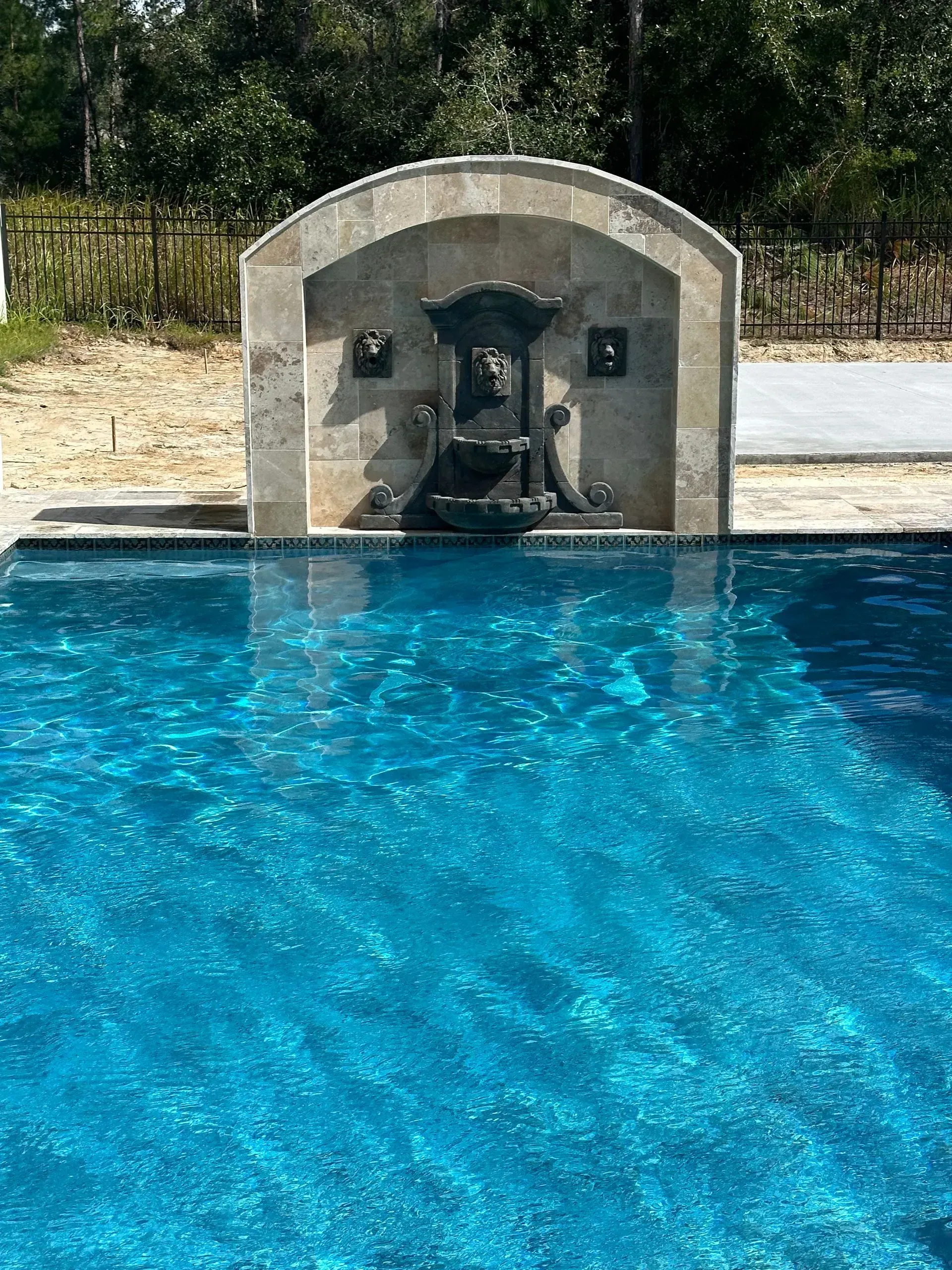 Stone fountain structure over a shimmering blue swimming pool.
