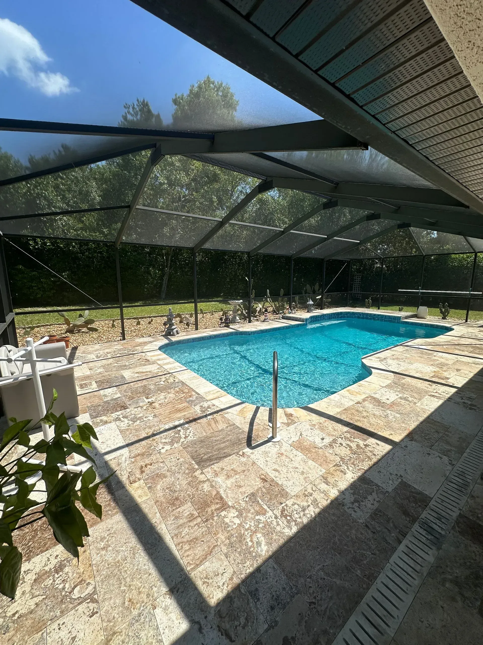Pool with screened enclosure; blue water, stone patio, green foliage in the background.