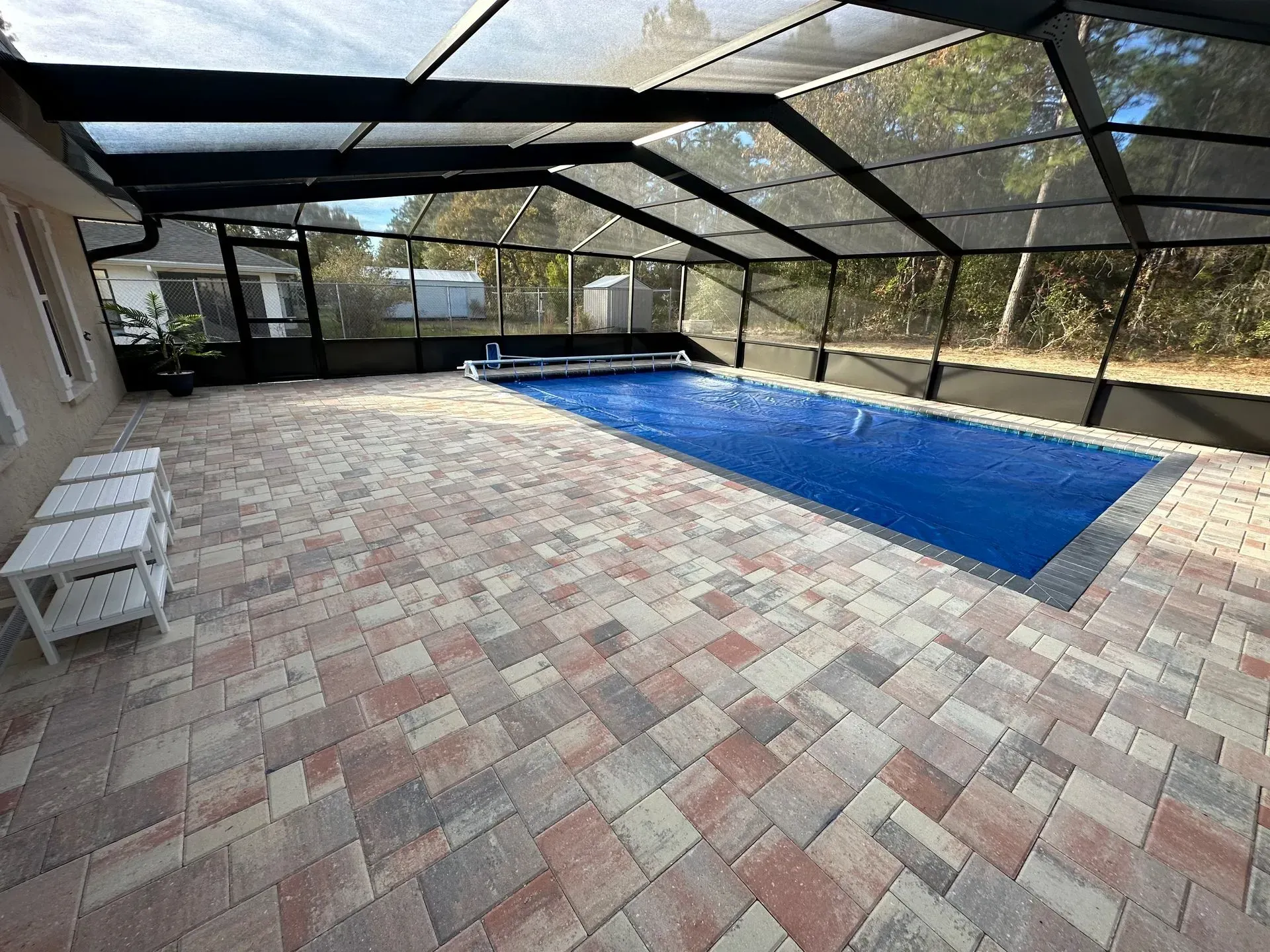 Patio enclosure with a pool covered by a blue tarp. Brick pavers and a screen enclosure.