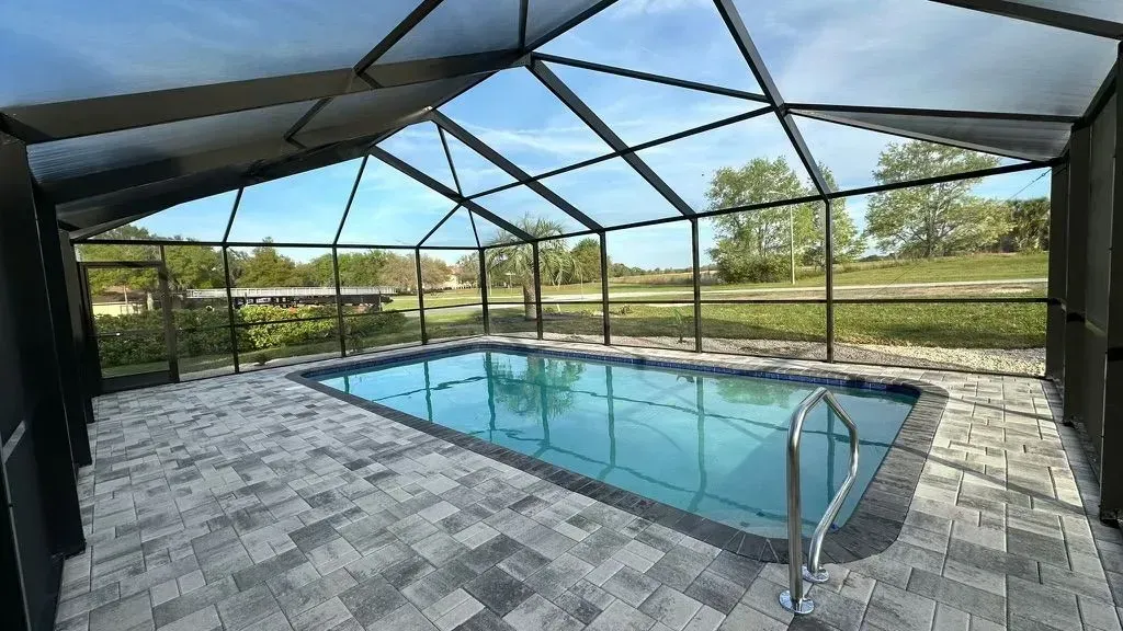 Pool enclosed in a screen structure; blue water, gray brick, clear sky.