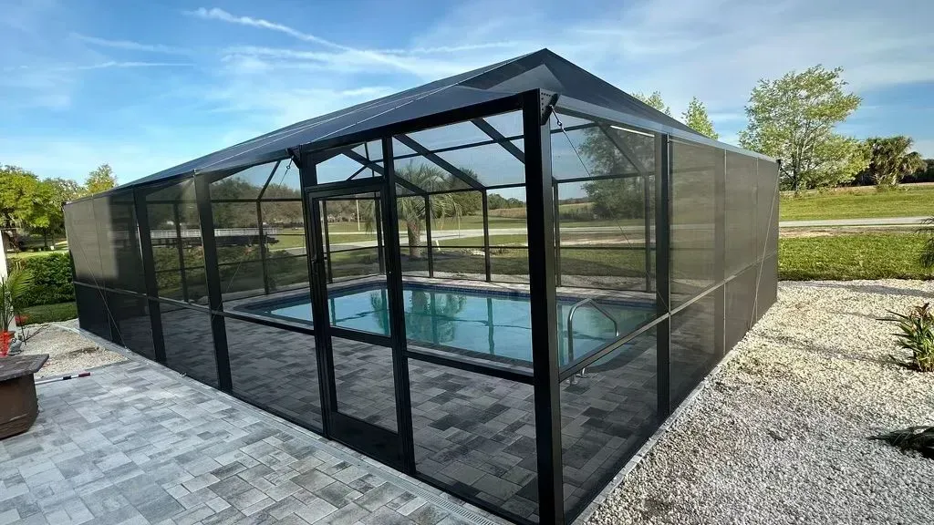 Screened-in black pool enclosure with clear water, on a stone patio with a blue sky background.