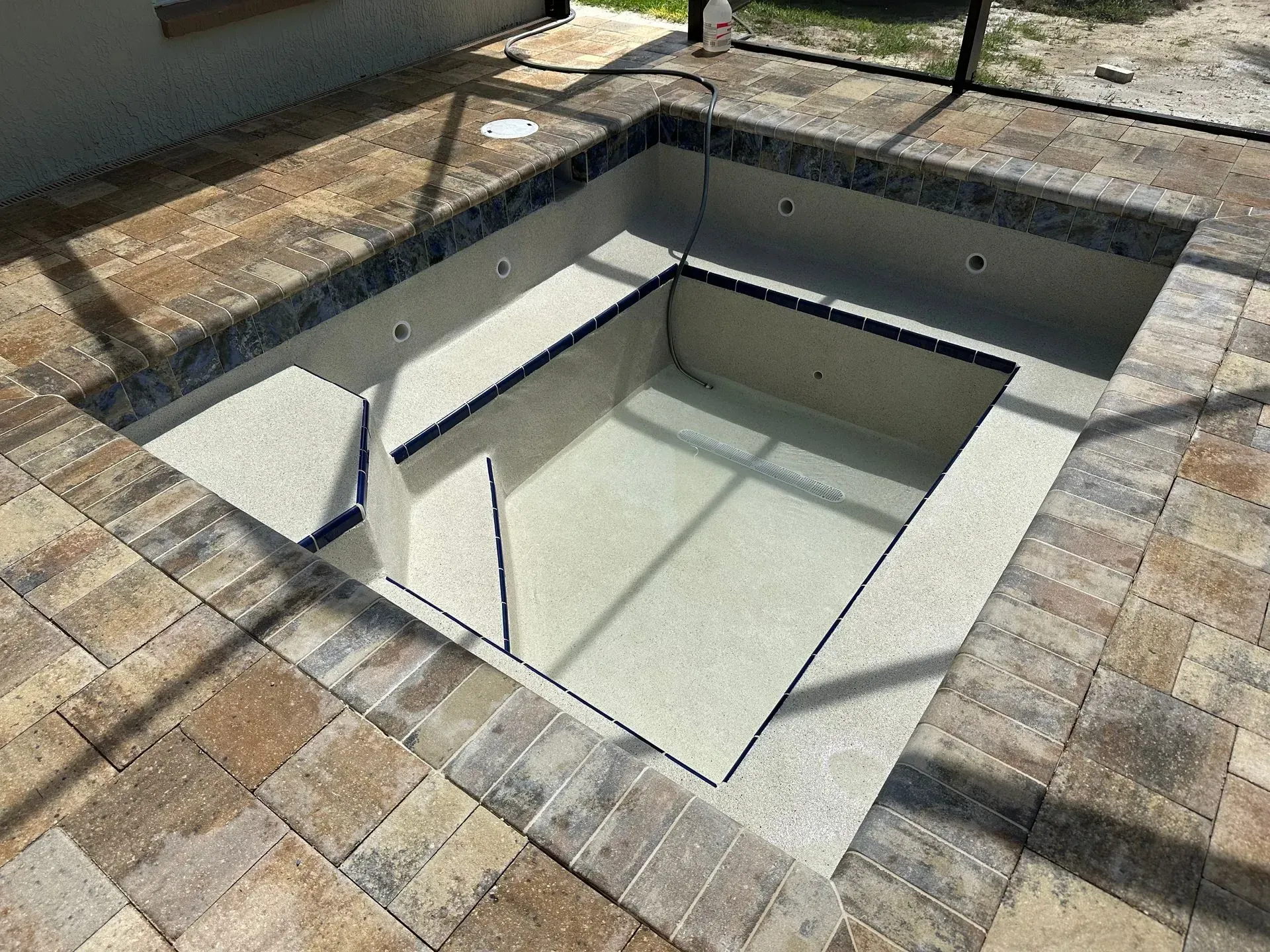 Empty in-ground pool with stone coping and brick patio.