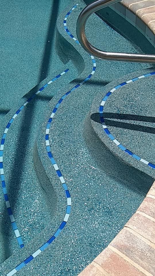 Pool steps with blue mosaic wave pattern and a stainless steel handrail.