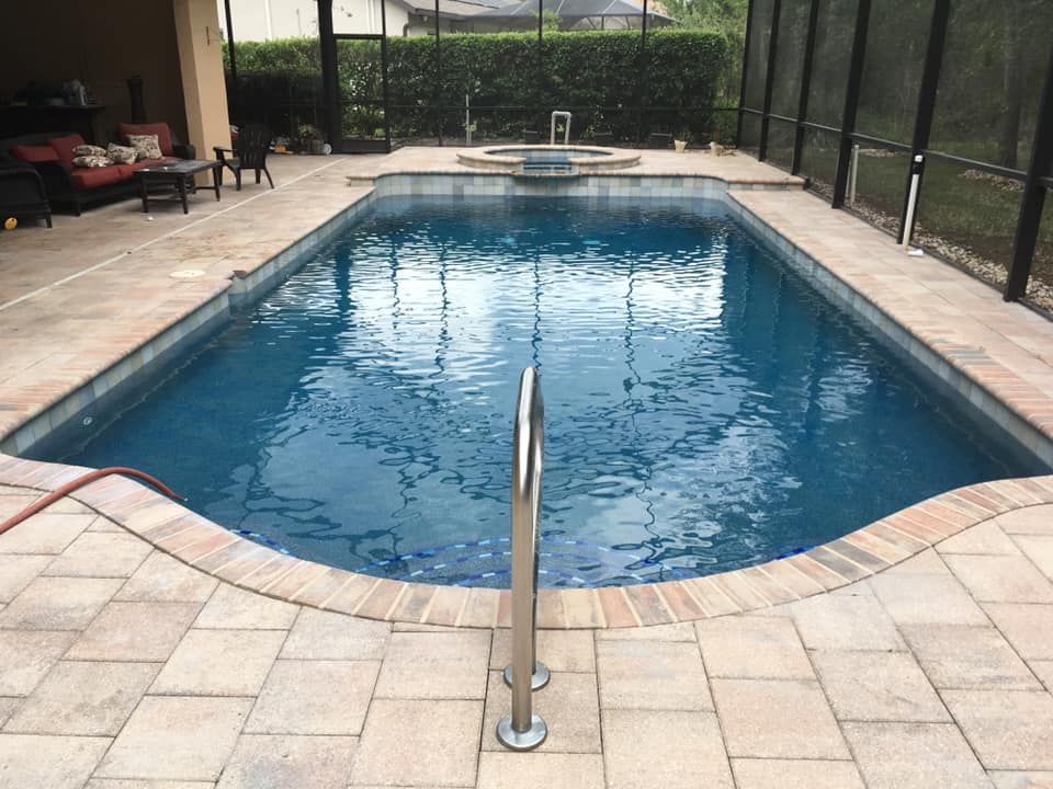 Swimming pool with brick pavers and handrail. Spa in the background, enclosed by a screen.