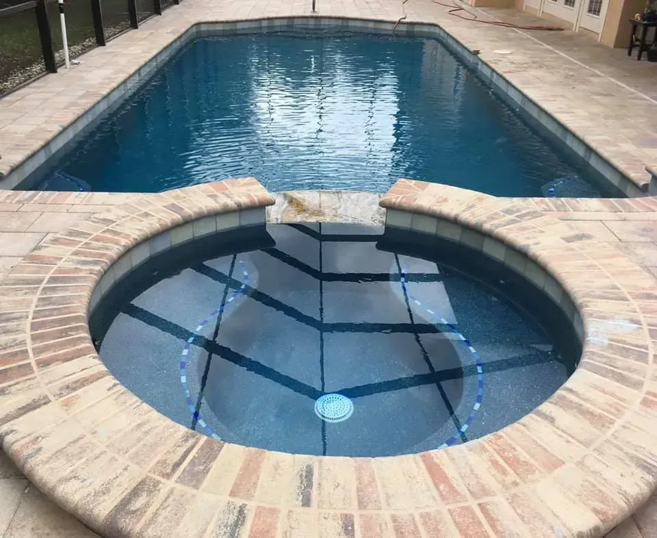 Pool and spa with blue water, surrounded by brick and stone patio.