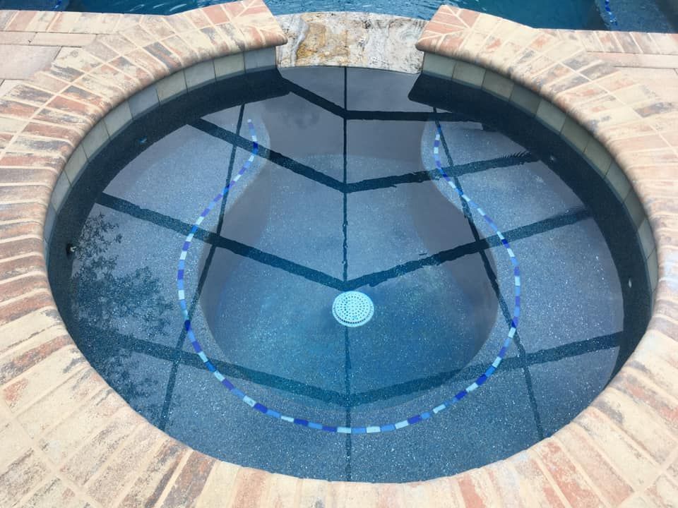 Circular spa with brick border, filled with blue water. Blue and white tile accent the floor.