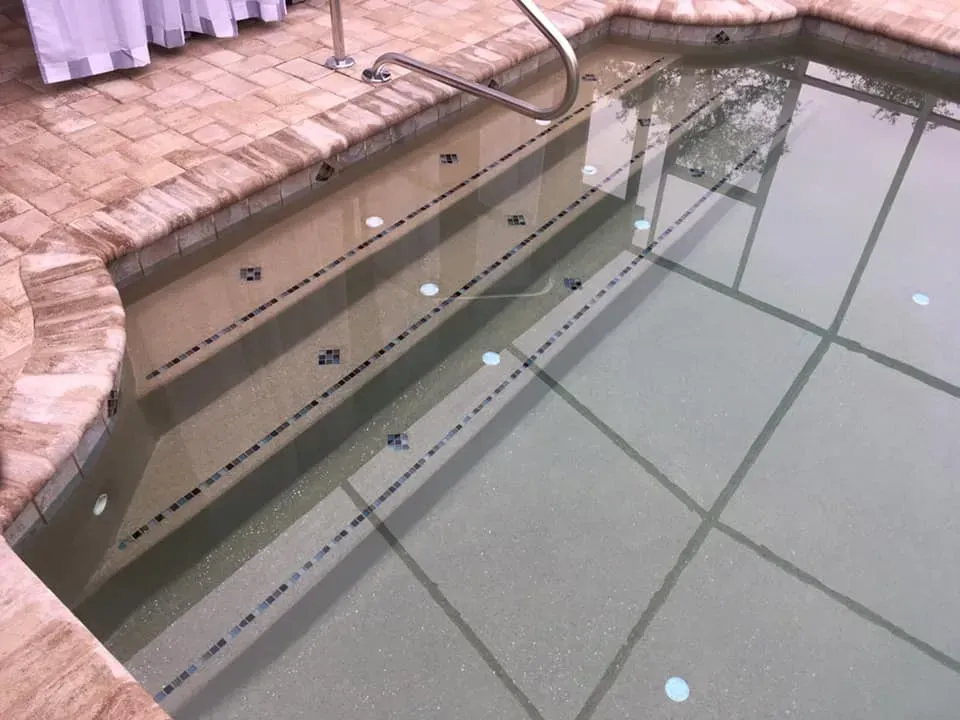 Swimming pool with steps and a handrail, brick border, and grid pattern on the bottom.