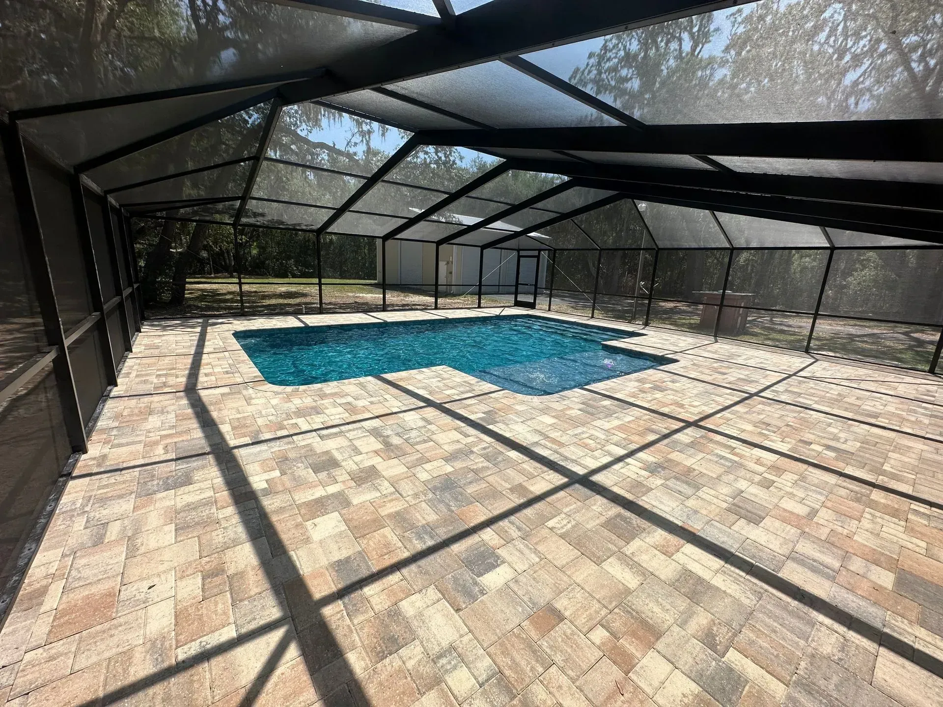 Screened-in pool area with pavers, a swimming pool, and a view of trees beyond.