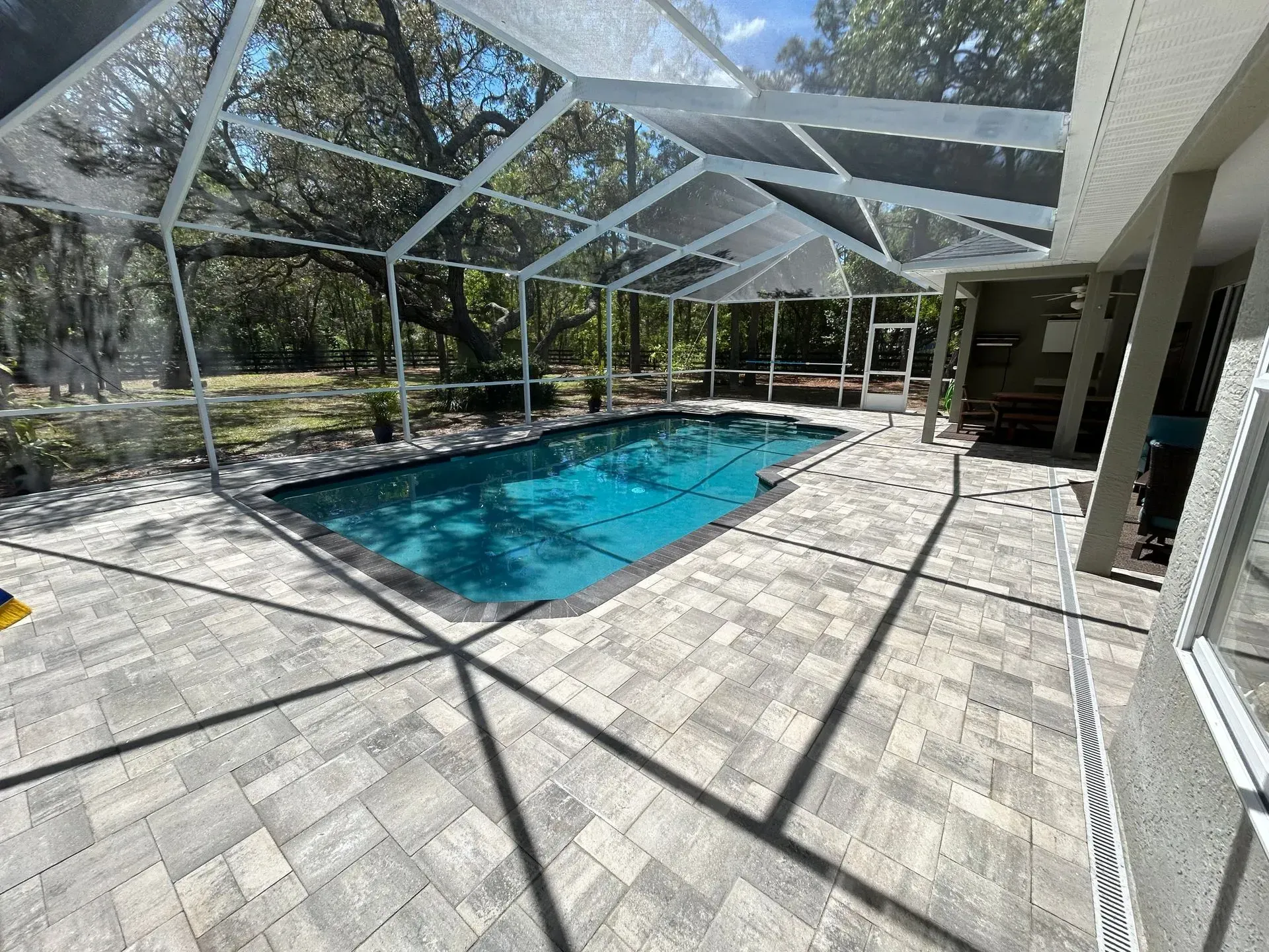 Pool enclosed by screen, surrounded by stone pavers, with trees in the background.
