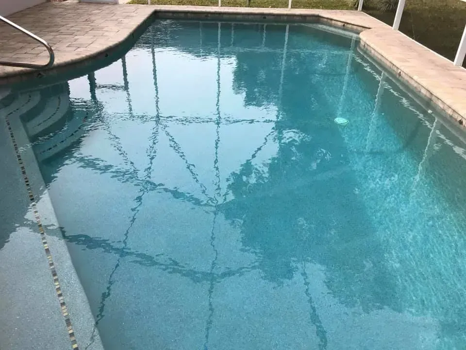Swimming pool with blue water, surrounded by concrete and a screened enclosure.