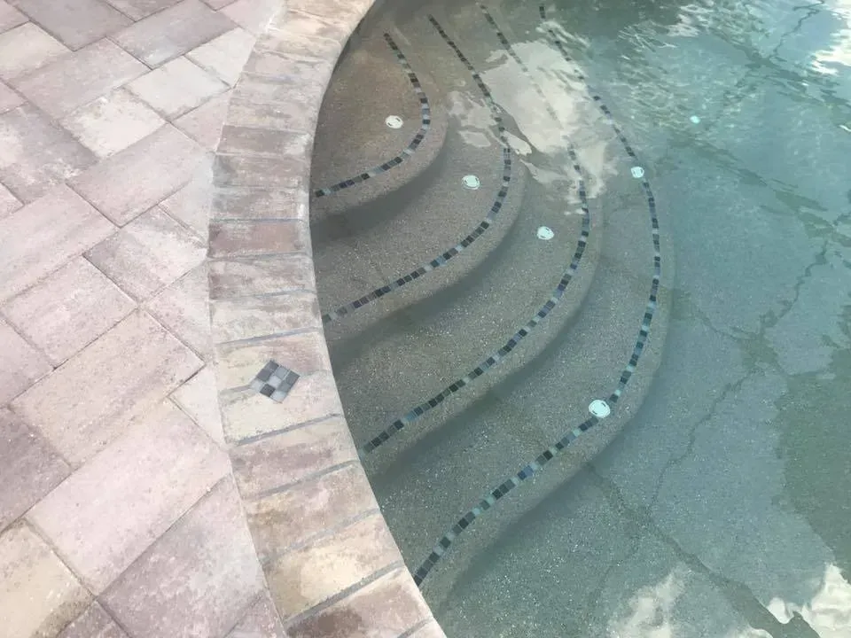 Curving pool steps with decorative tile and brick edging. Steps lead into clear water.