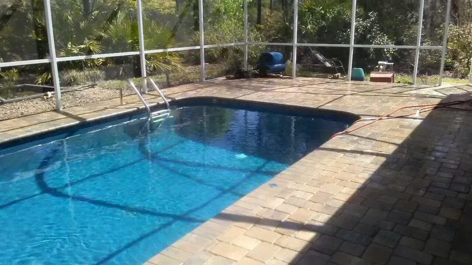 Swimming pool with blue water, brick deck, and screened enclosure.