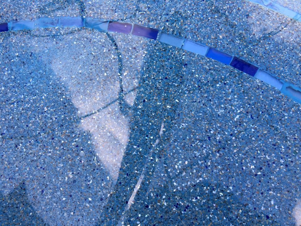 Pool water with blue tile edging, dappled sunlight creates shadows.