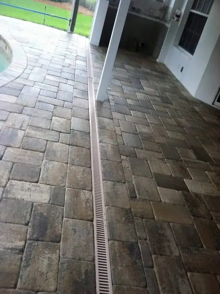 Brick patio with drainage channel, beside a pool and covered patio.