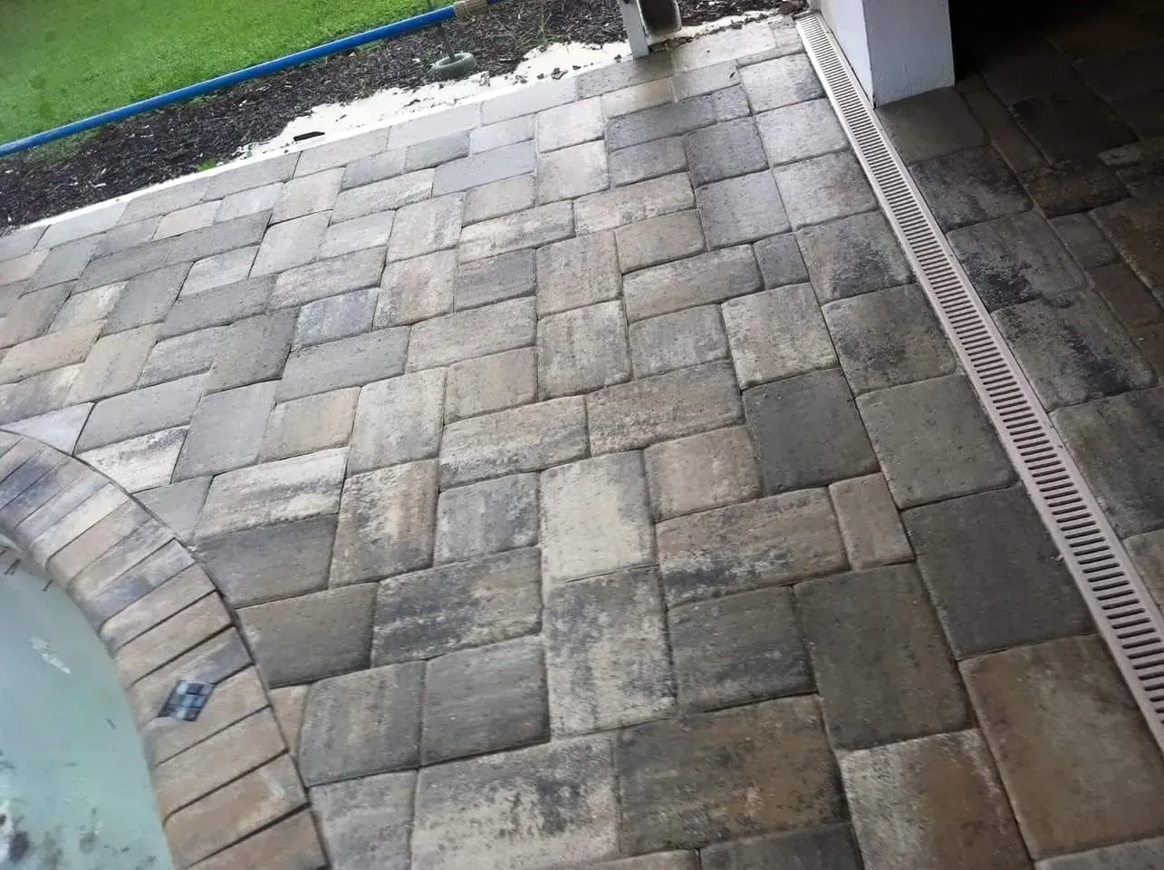 Patio paved with rectangular gray and brown bricks, alongside a curved edge and a drainage gutter.