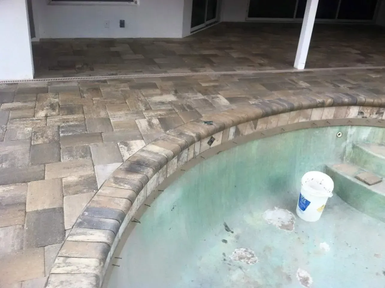 Pool with brick coping and surrounding pavers, white bucket inside.