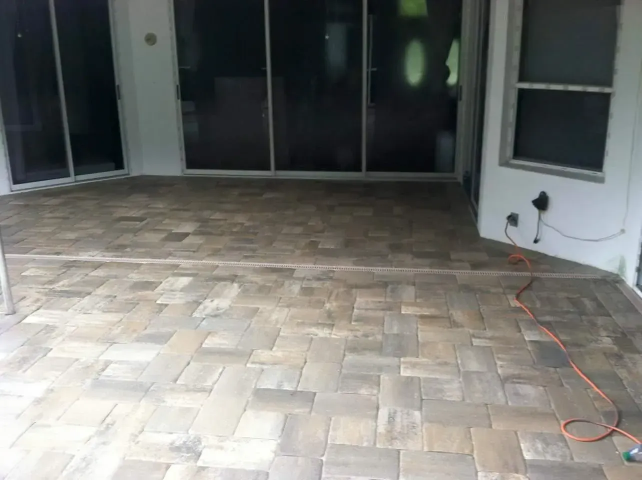Patio paved with rectangular bricks, in front of glass doors and a white wall, orange electrical cord visible.