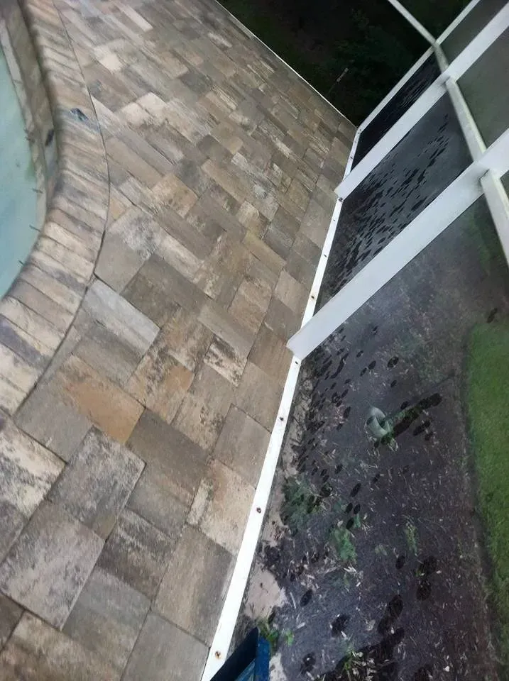 Poolside patio with brick pavers next to a fence and a pool.