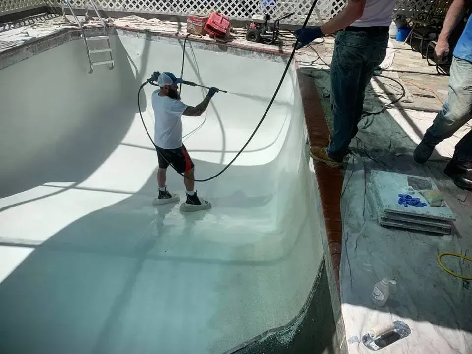A person power washing the interior of a concrete swimming pool.