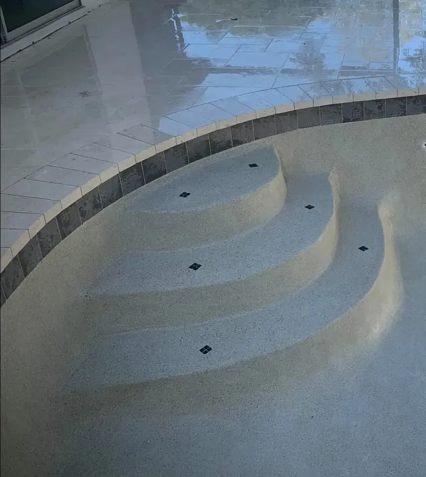 Curved pool steps with dark border, tan steps, and light gray pool bottom, surrounded by light gray concrete.