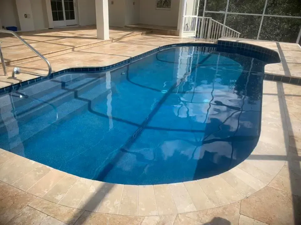 A blue swimming pool with a mosaic tile interior, surrounded by beige tiling.