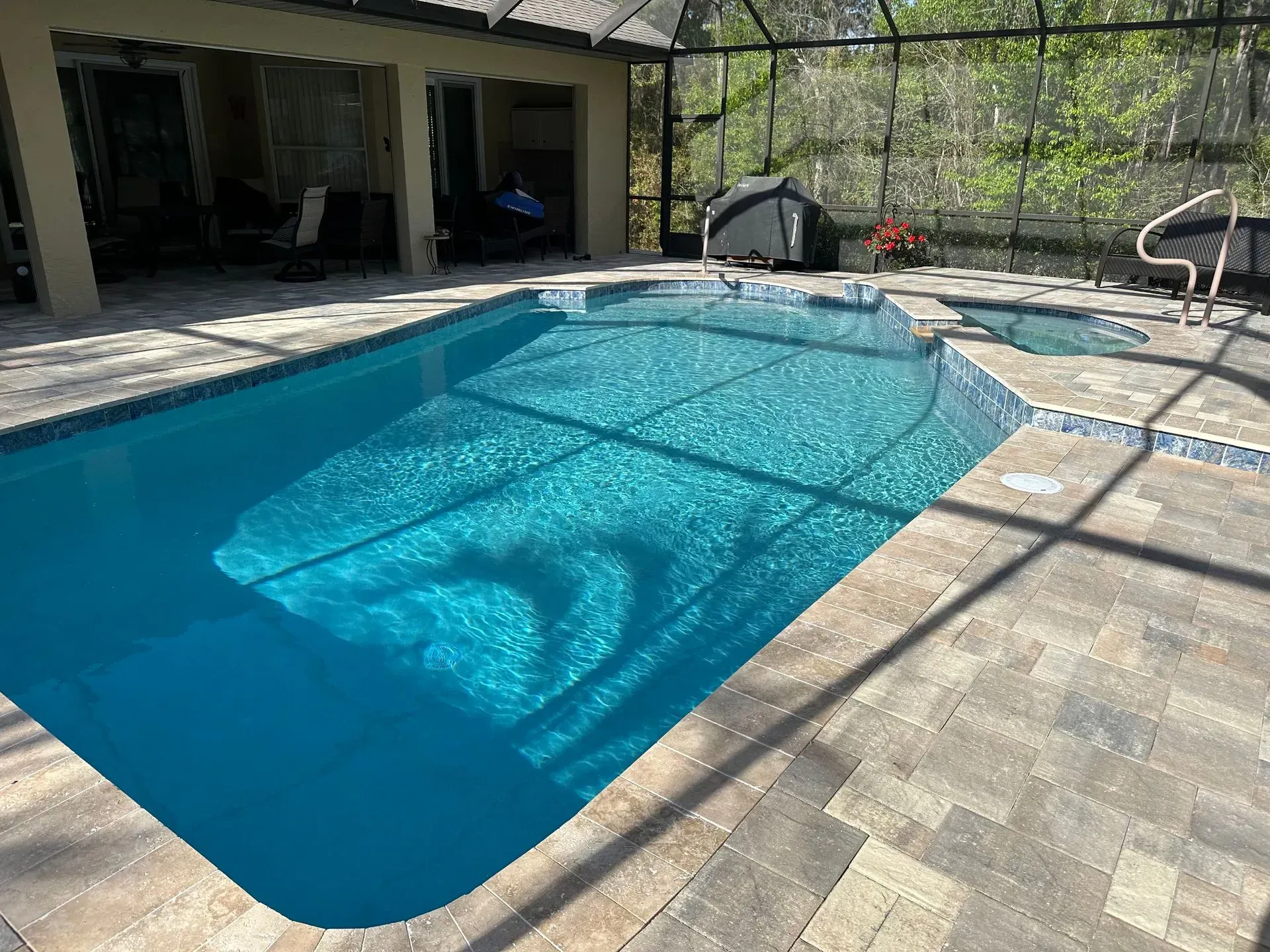 Blue swimming pool and spa with brick patio, under a screened enclosure.