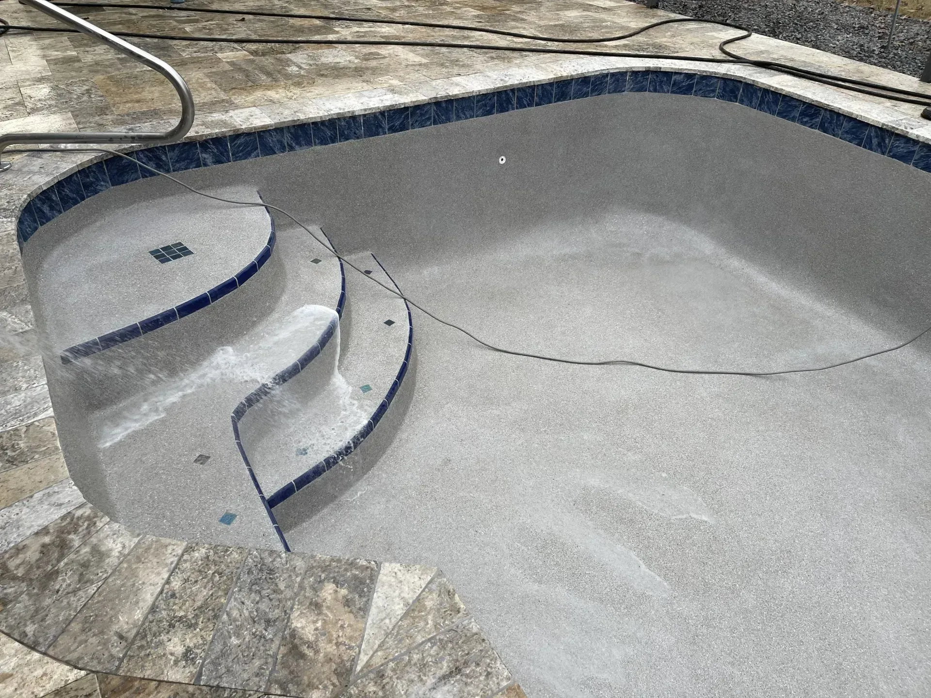 Empty swimming pool with steps, blue tile trim, and gray speckled interior.