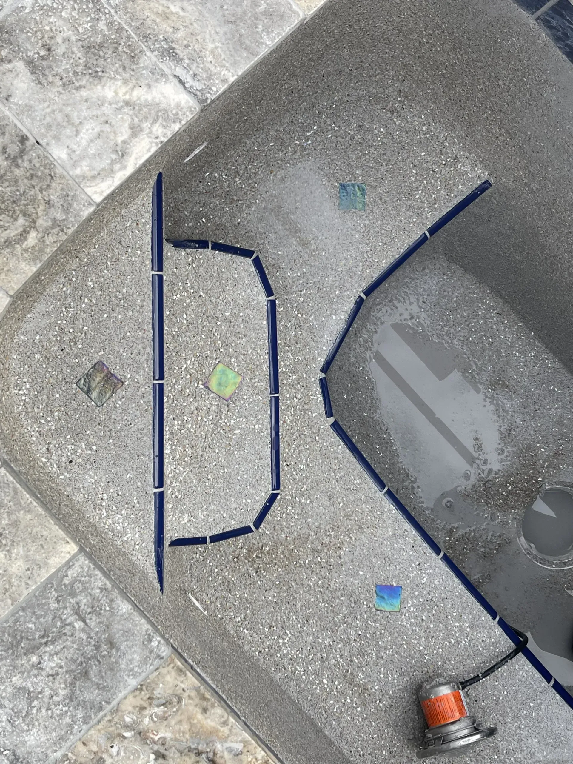 Dark blue tile outline on gray concrete pool edge. Electric tool at the bottom.