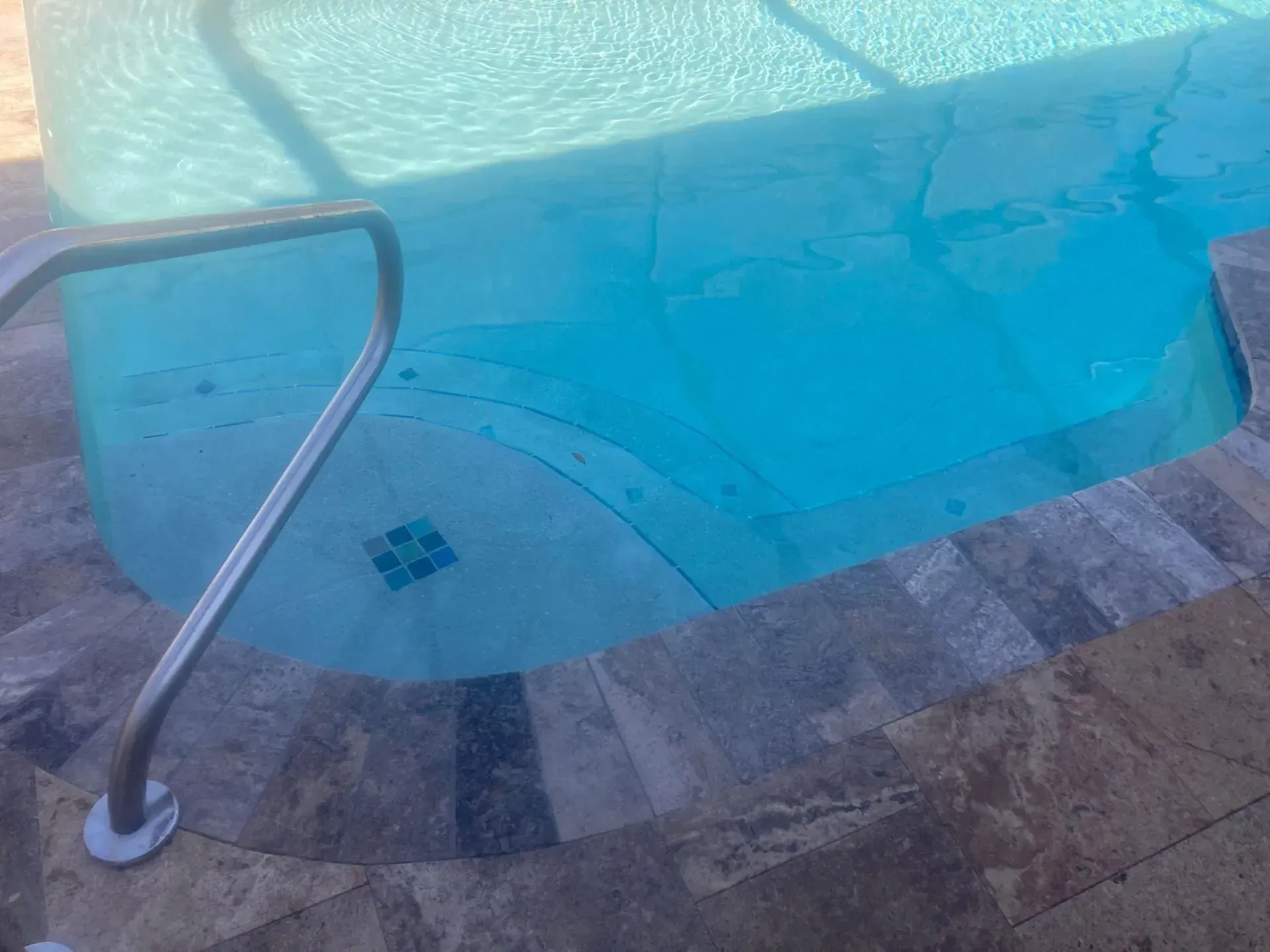 Pool with light blue water and stone edge, a metal handrail, and small blue tiles.
