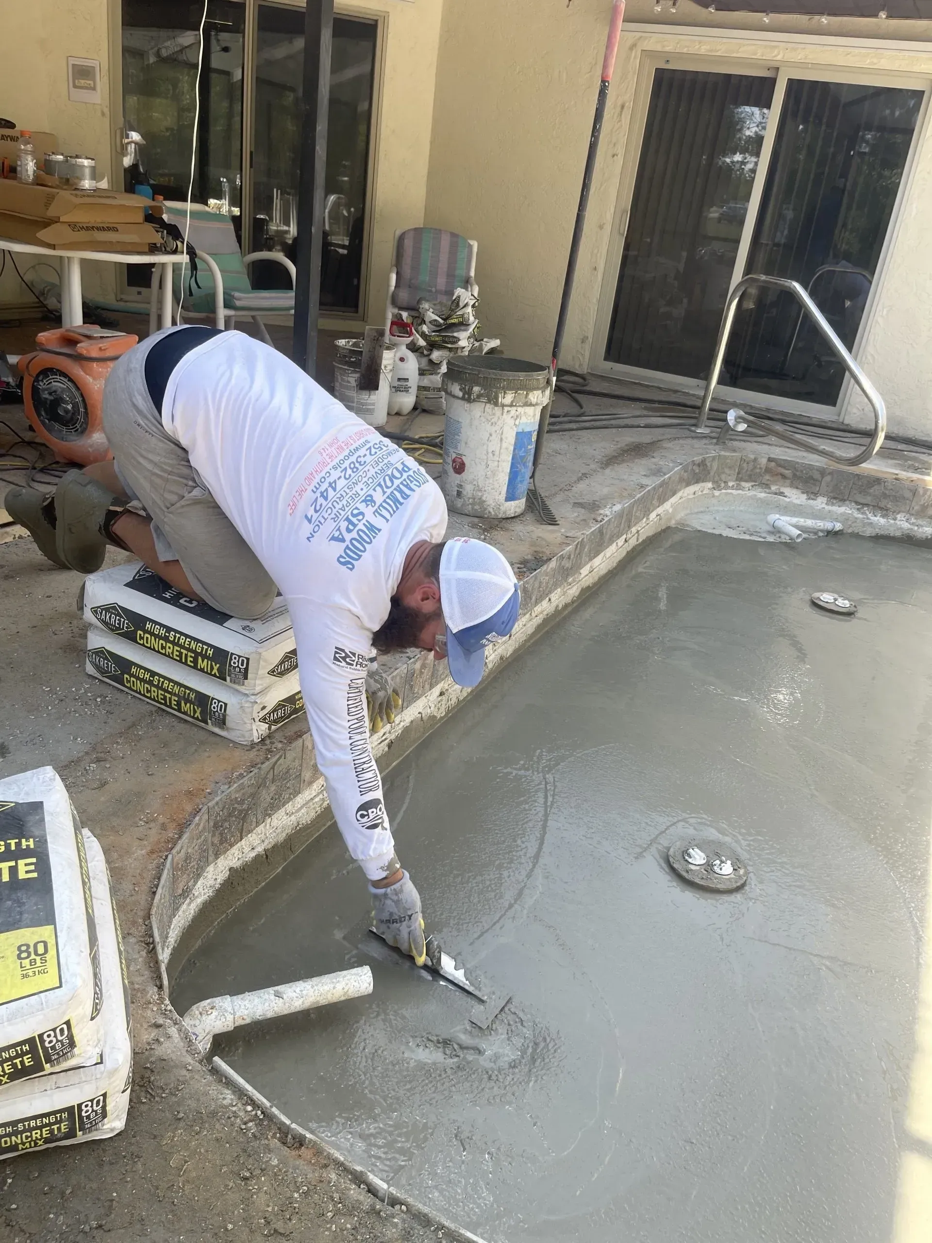Man smoothing wet concrete in a pool with a trowel, outdoors.