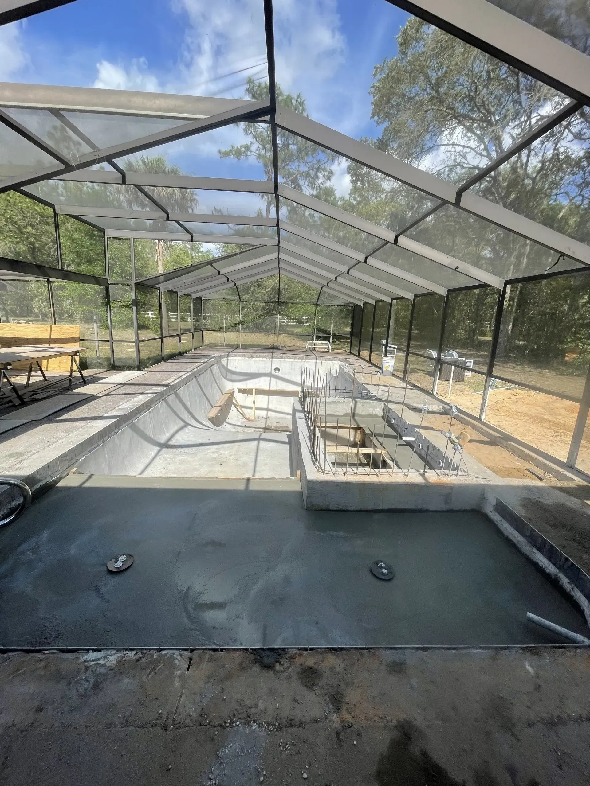 Pool under construction enclosed by a screen structure, concrete work visible.