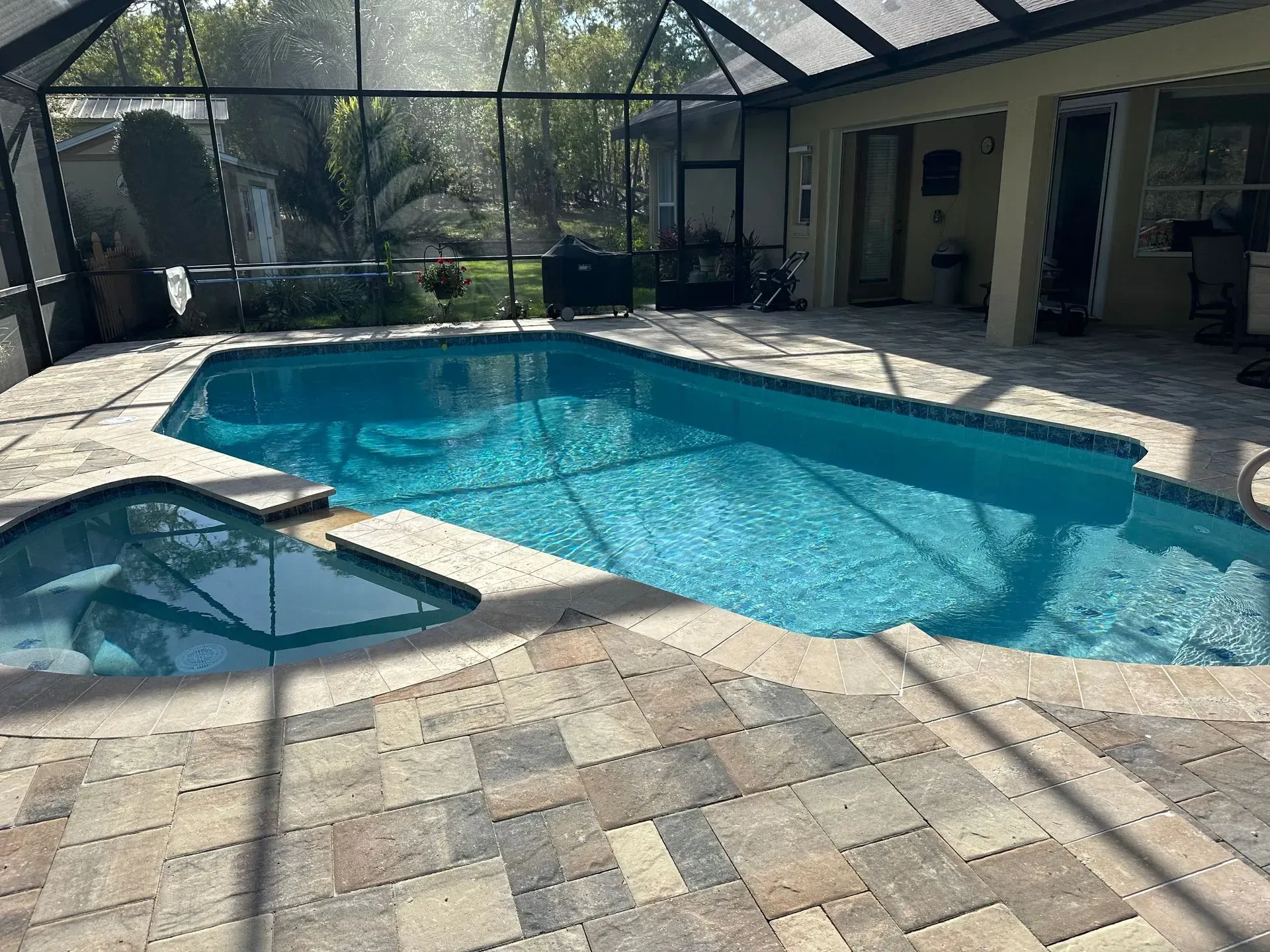 Pool with blue water surrounded by stone pavers, under a screened enclosure.