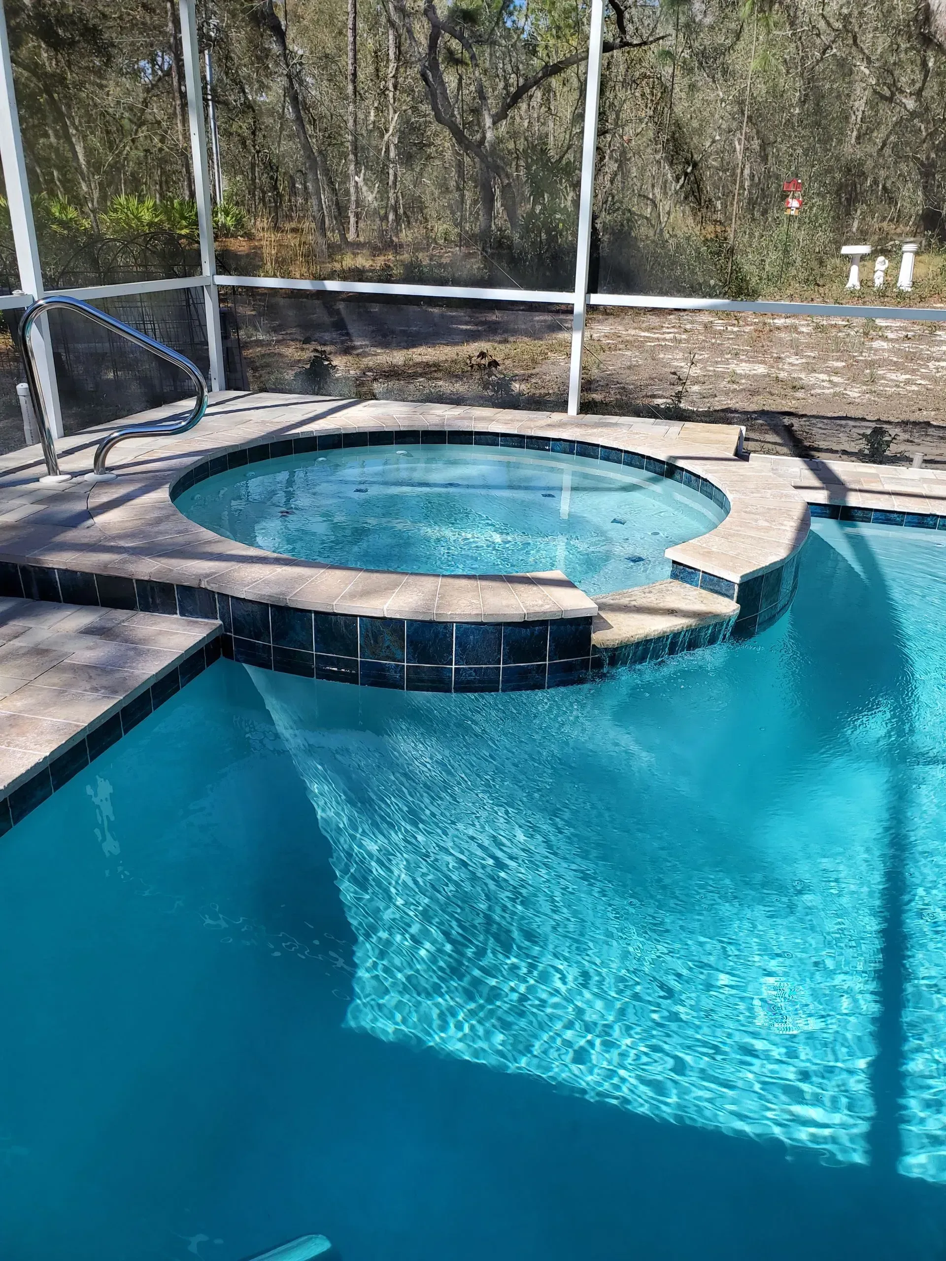 Swimming pool with attached circular hot tub, both filled with blue water.