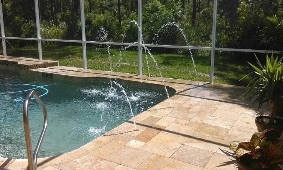 Pool with fountains spraying water, surrounded by a screened enclosure and patio.