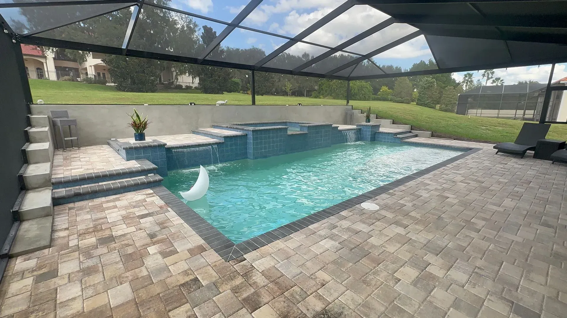 Pool with waterfall feature and screened enclosure, surrounded by stone patio.