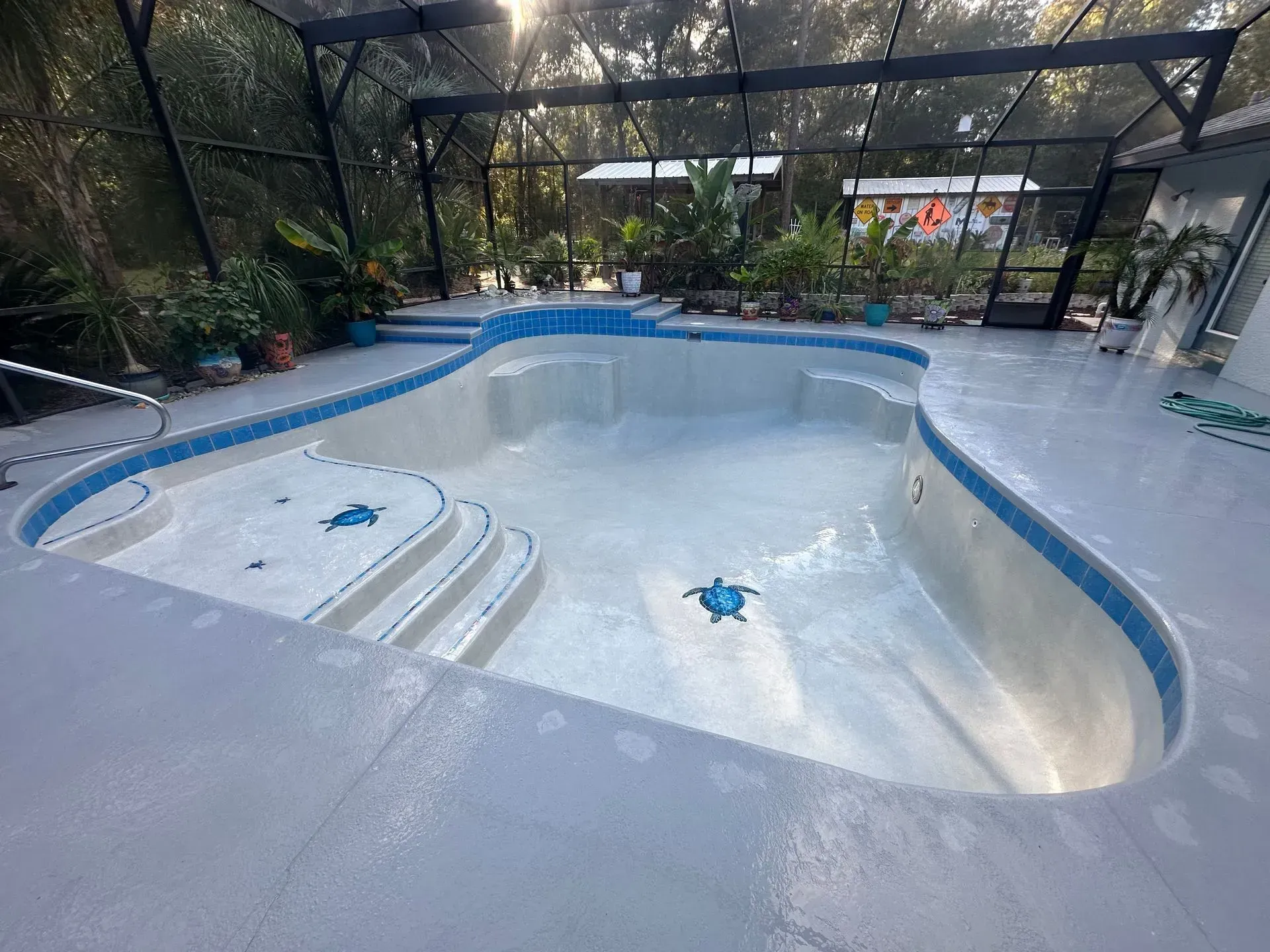 Empty, light-blue tiled swimming pool in an outdoor screened-in enclosure.