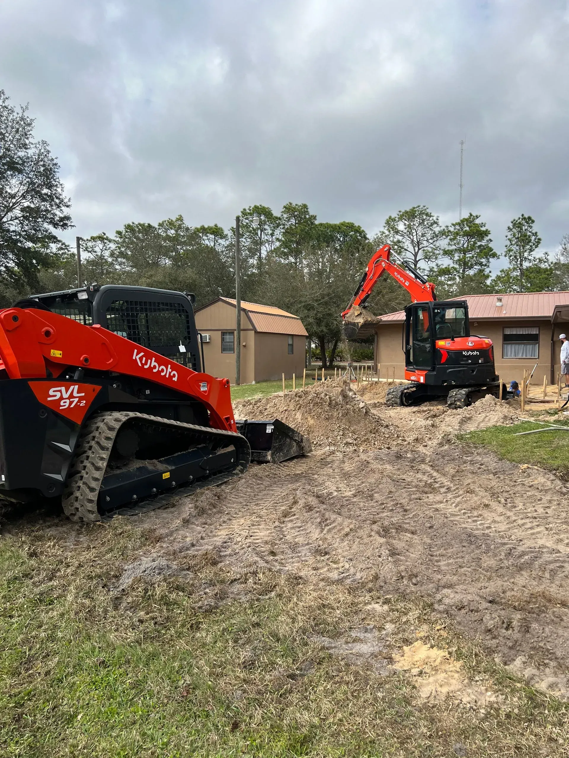 Two Kubota construction machines working on dirt near a building.